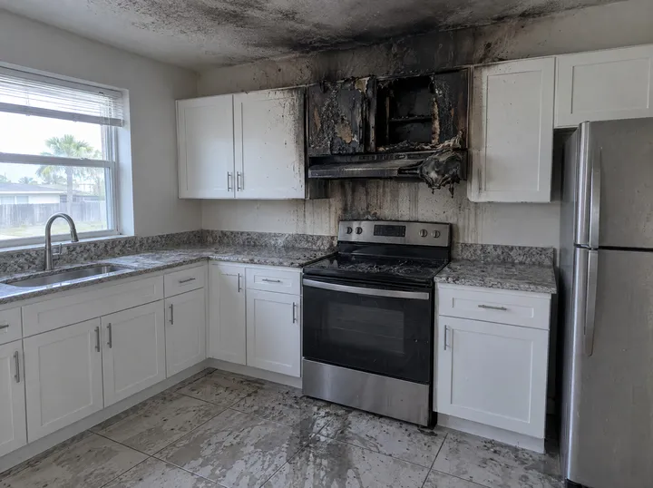 Kitchen after a fire: soot on the wall and ceiling, a charred cabinet above the stove.